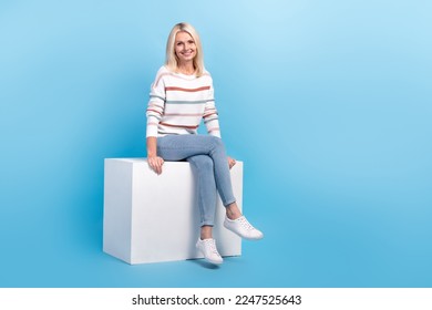 Full length photo of stunning lady wear new clothes sitting cube presenting cool novelty empty space isolated on blue color background - Shutterstock ID 2247525643
