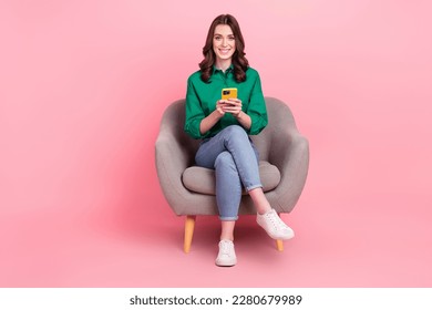 Full length photo of sweet cheerful woman wear green shirt sitting couch texting modern gadget isolated pink color background - Powered by Shutterstock