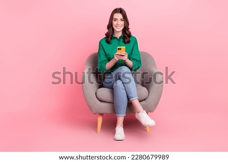 Full length photo of sweet cheerful woman wear green shirt sitting couch texting modern gadget isolated pink color background
