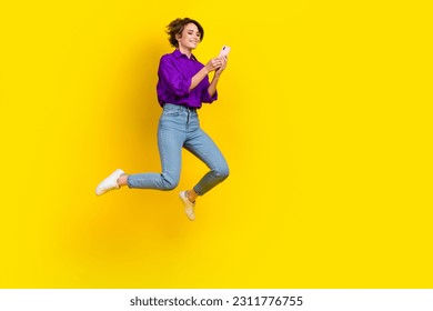Full length photo of sweet cute lady wear violet shirt jumping chatting samsung iphone apple device isolated yellow color background