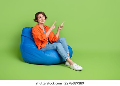 Full length photo of sweet dreamy lady dressed jeans shirt bean bag showing emtpy space isolated green color background