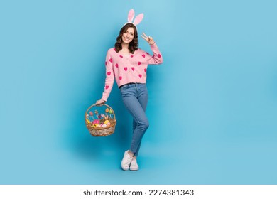 Full length photo of sweet friendly woman wear pink cardigan enjoying easter showing v-sign emtpy space isolated blue color background