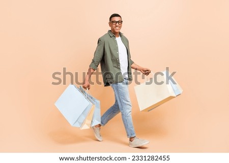 Full length photo of sweet handsome man wear khaki shirt walking holding bargains isolated beige color background
