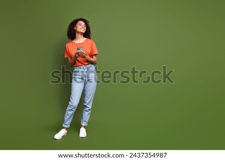 Full length photo of sweet shiny lady dressed orange t-shirt typing modern device looking empty space isolated khaki color background