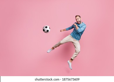Full length photo of sweet strong young man dressed blue sweater jumping high kick foot ball isolated pink color background