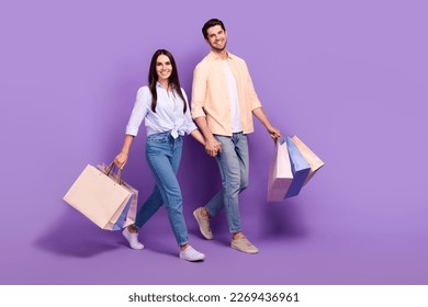 Full length photo of two cheerful lovely partners walk shopping hold arms isolated on violet color background
