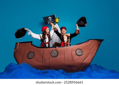 Full length photo of two little kids raise hats celebrate dressed pirates costumes birthday party playing ship isolated on blue background - Powered by Shutterstock