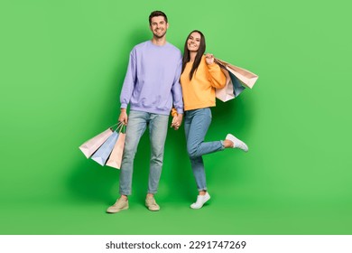 Full length photo of two lovely partners toothy smile hold hands shop packages isolated on green color background