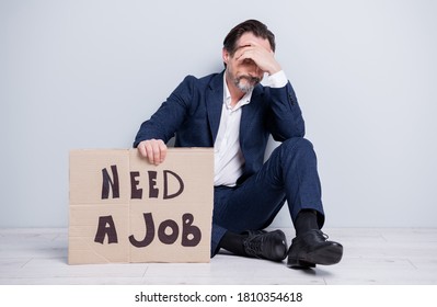 Full length photo of unhappy disappointed worker mature guy lost work jobless man hold carton placard seek work sit floor hide eyes look wear blue suit shoes isolated grey background