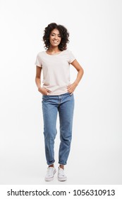 Full Length Photo Of Vivacious American Woman Wearing Jeans And T-shirt Posing On Camera With Candid Smile And Hands In Pocket Isolated Over White Background