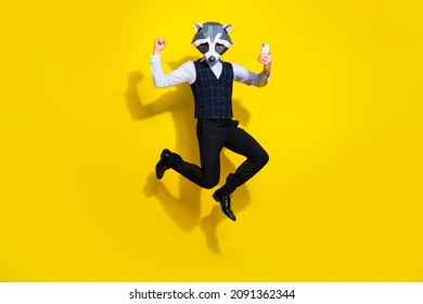 Full length photo of weird guy racoon mask jump raise fist up use device wear stylish trend vest isolated over yellow color background - Shutterstock ID 2091362344
