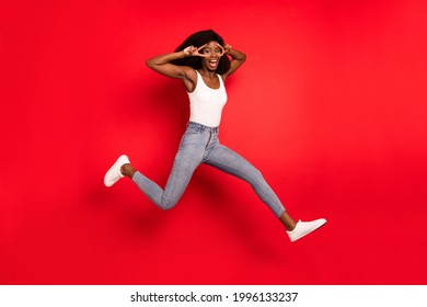 Full Length Photo Of Young Afro Girl Happy Positive Smile Jump Up Show Peace Cool V-sign Isolated Over Red Color Background