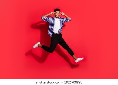 Full length photo of young black guy happy smile show peace cool v-sign jump isolated over red color background
