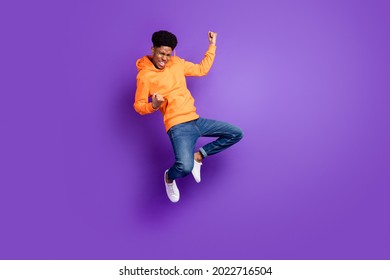 Full length photo of young crazy dark skin man jump up air fists winner celebrate isolated on violet color background