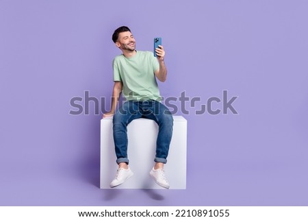 Full length photo of young guy hold gadget sit cube instagram telegram twitter facebook wear gray look isolated on violet color background