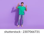 Full length photo of young man greetings symbol showing v-sign hello wear green t-shirt denim carhartt jeans isolated on violet background