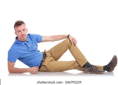 full length picture of a casual young man lying on the floor and looking into the camera with a serious expression on his face. on a white background