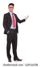 Full Length Picture Of A Young Business Man Presenting Something In The Back With One Hand In His Pocket While Looking At The Camera With A Smile On His Face, On White Background