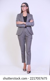 Full Length Picture Of A Young Entrepreneur Woman Looking Away From Camera With Crossed Arms. Successful Business Woman Walking Forward In A Formal Suite With Specs. Isolated On White Background 