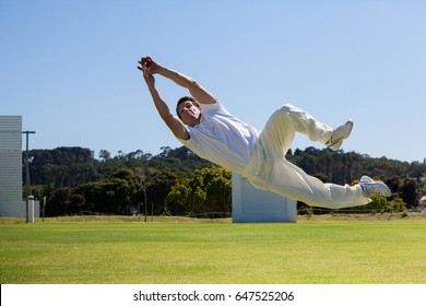 Full length of player diving to catch ball against blue sky over field
