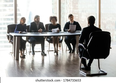 Extensión completa simpática sonriente multirracial diversos gestores de recursos humanos sentados a la mesa a distancia de un candidato masculino, haciendo preguntas sobre experiencia laboral, concepto de contratación de primera impresión.