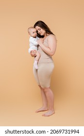 Full Length Of Plus Size Mother Holding Baby Daughter On Beige Background