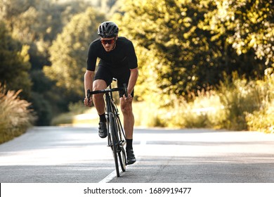 Full Length Portrait Of Active Man In Sport Clothing And Protective Helmet Riding Bike With Blur Background Of Summer Nature. Concept Of Workout And Races.