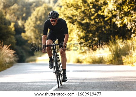 Full length portrait of active man in sport clothing and protective helmet riding bike with blur background of summer nature. Concept of workout and races.