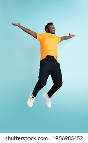 Full length portrait of African young man isolated over blue studio background with copyspace for ad. Male fashion model in yellow shirt. Concept of human emotions, facial expression, youth culture.