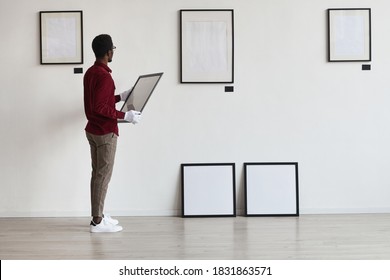 Full Length Portrait Of African-American Man Planning Art Gallery Or Exhibition While Setting Up Frames On White Wall, Copy Space