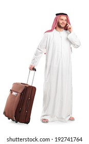 Full length portrait of an Arabic sheik talking on phone and carrying a luggage isolated on white background