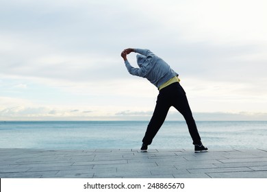 Full length portrait of a athletic man stretching in the morning and admiring beautiful view while  standing next to the sea