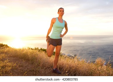 Full Length Portrait Of Athletic Woman Stretching Outdoors By Sunset