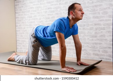 Full Length Portrait Of Attractive Man Working Out At Home In Living Room, Doing Yoga Or Pilates Exercise On Mat. Cow Posture, Asana Paired With Cat Pose On The Exhale. Side View