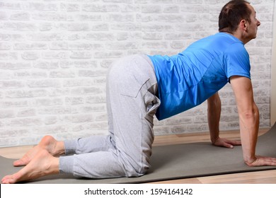 Full Length Portrait Of Attractive Man Working Out At Home In Living Room, Doing Yoga Or Pilates Exercise On Mat. Cow Posture, Asana Paired With Cat Pose On The Exhale. Side View