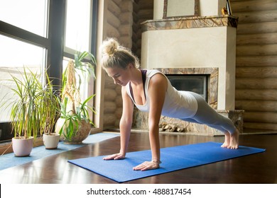 Full length portrait of attractive young woman working out at home in living room, doing yoga or pilates exercise on blue mat, standing in plank pose (phalankasana) - Powered by Shutterstock