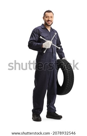 Full length portrait of an auto mechanic holding a tire and a lug wrench isolated on white background