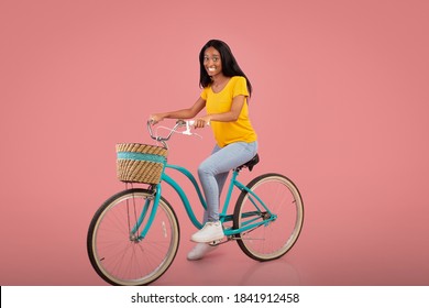 Full Length Portrait Of Beautiful African American Woman Riding Vintage Bicycle Over Pink Studio Background. Positive Black Lady On Bike Going Cycling, Enjoying Her Ride. Active Lifestyle Concept