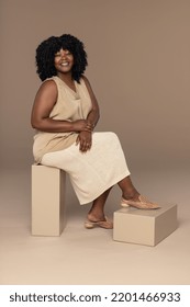 Full length portrait of a beautiful African American woman in her 30's posed sitting on blocks on a neutral background Stock Photo