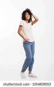 Full length portrait of beautiful american woman wearing jeans and t-shirt posing on camera with candid smile and hand in pocket isolated over white background