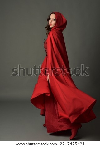 Full length portrait of beautiful brunette woman wearing red medieval fantasy costume with long skirt and flowing hooded cloak.
Standing pose in back view with gestural hand poses, walling away from c