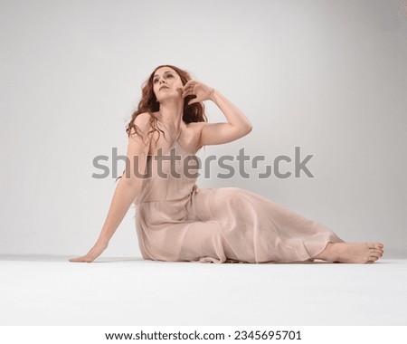 Full length portrait of beautiful brunette model  wearing a  pink dress. graceful sitting  pose, kneeling on floor gestural hands. shot from low angle perspective,  isolated on white studio background