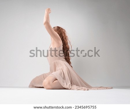 Full length portrait of beautiful brunette model  wearing a  pink dress. graceful sitting  pose, kneeling on floor gestural hands. shot from low angle perspective,  isolated on white studio background