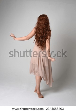 Full length portrait of beautiful  female model with long  brunette hair wearing a creamy pink gown dress. graceful dancing pose, with gestural hands  isolated on white studio background.
