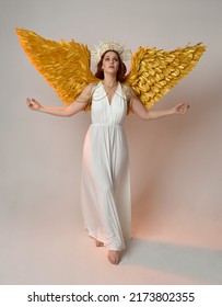 Full length portrait of beautiful red head woman wearing long flowing fantasy toga gown with golden halo crown jewellery, standing pose   isolated on a white studio background.