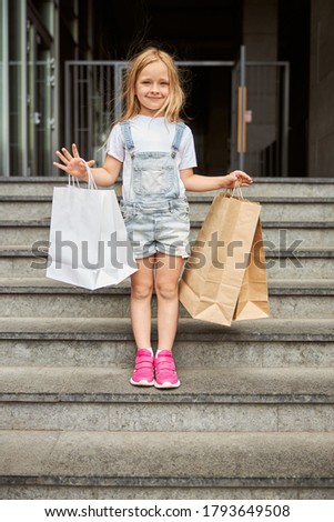 Full length portrait of beautiful smiling little girl holding paper shopping bags while standing on the steps in the outdoors