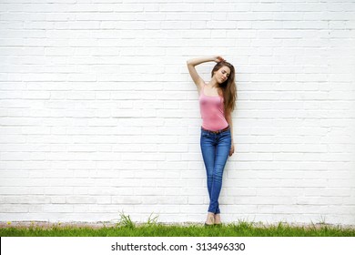 Full length portrait of a beautiful woman in blue jeans against a white brick wall