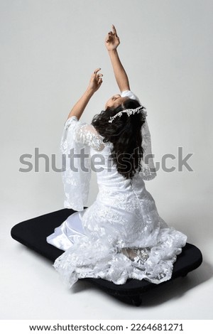 Full length  portrait of beautiful woman wearing  fantasy costume with white  lace bridal gown. Sitting pose with gestural arm movements reaching out as if casting a spell. Isolated on white studio ba