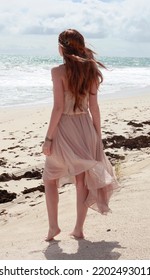 full length portrait of beautiful young woman with long hair wearing flowing dress, standing pose walking away from the camera.  ocean beach background with sunset lighting. - Shutterstock ID 2202493011
