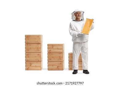 Full length portrait of a bee keeper in a uniform holding a honeybee frame in front of wooden boxes isolated on white background